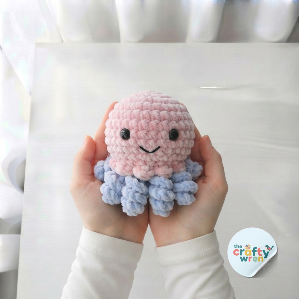 Finished amigurumi octopus crochet pattern held in two hands, pink head and eight curled pastel blue tentacles complete