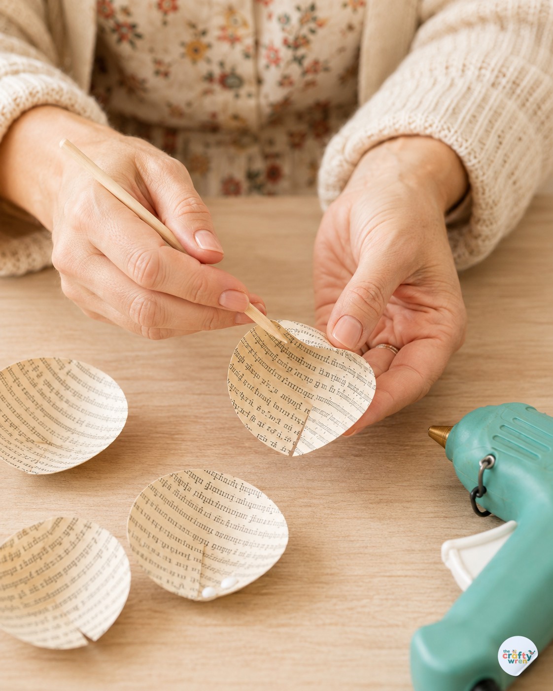 Hands curling paper petals with a wooden skewer while making book page paper roses