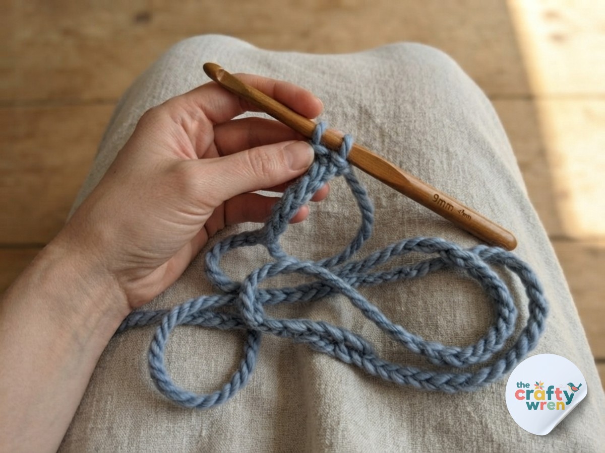 Hands crocheting a long foundation chain in chunky yarn, the very first step of the easy textured crochet blanket.