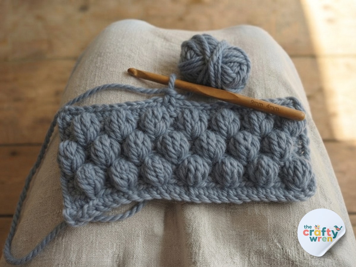 Two staggered rows of puff stitch flowers growing into the easy textured crochet blanket fabric on the hook.