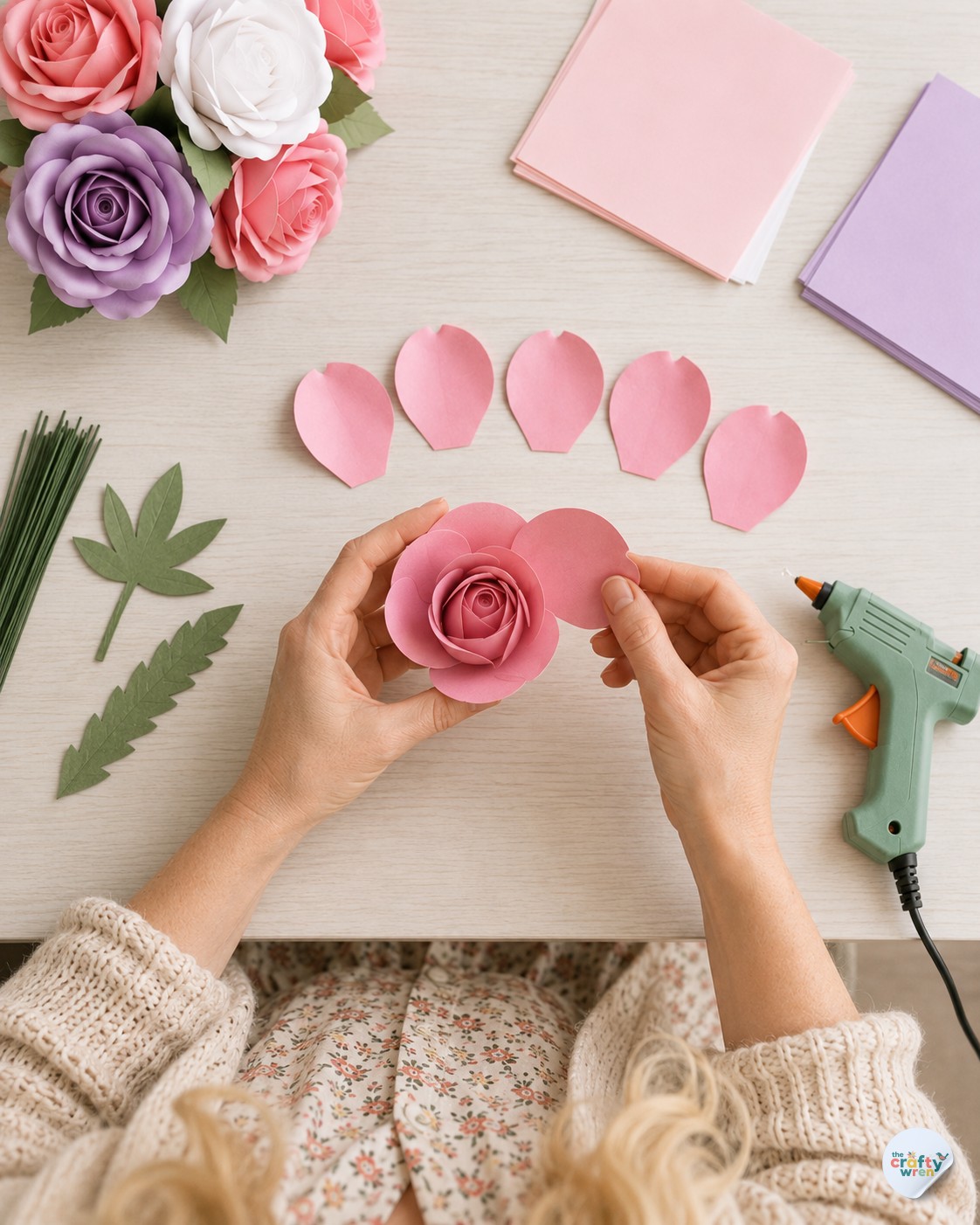 Overhead view of hands adding pink middle petals to a paper rose during bouquet assembly