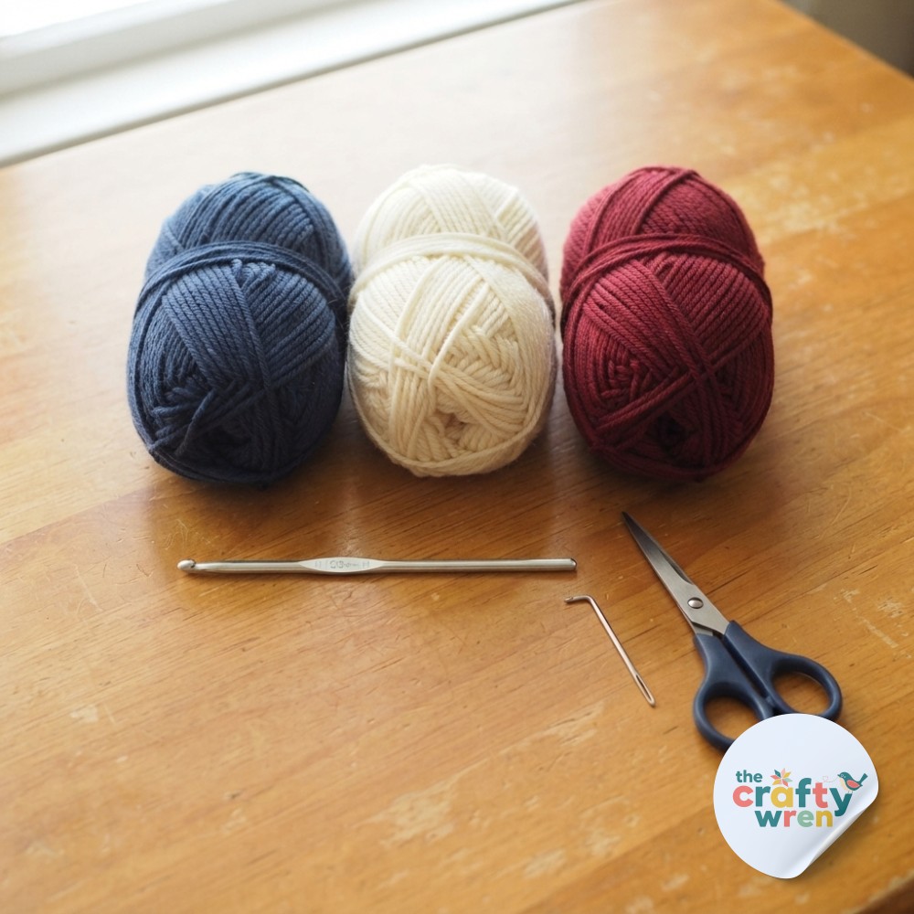 Navy, cream, and burgundy yarn plus a hook and scissors ready to start a striped one row repeat crochet blanket.